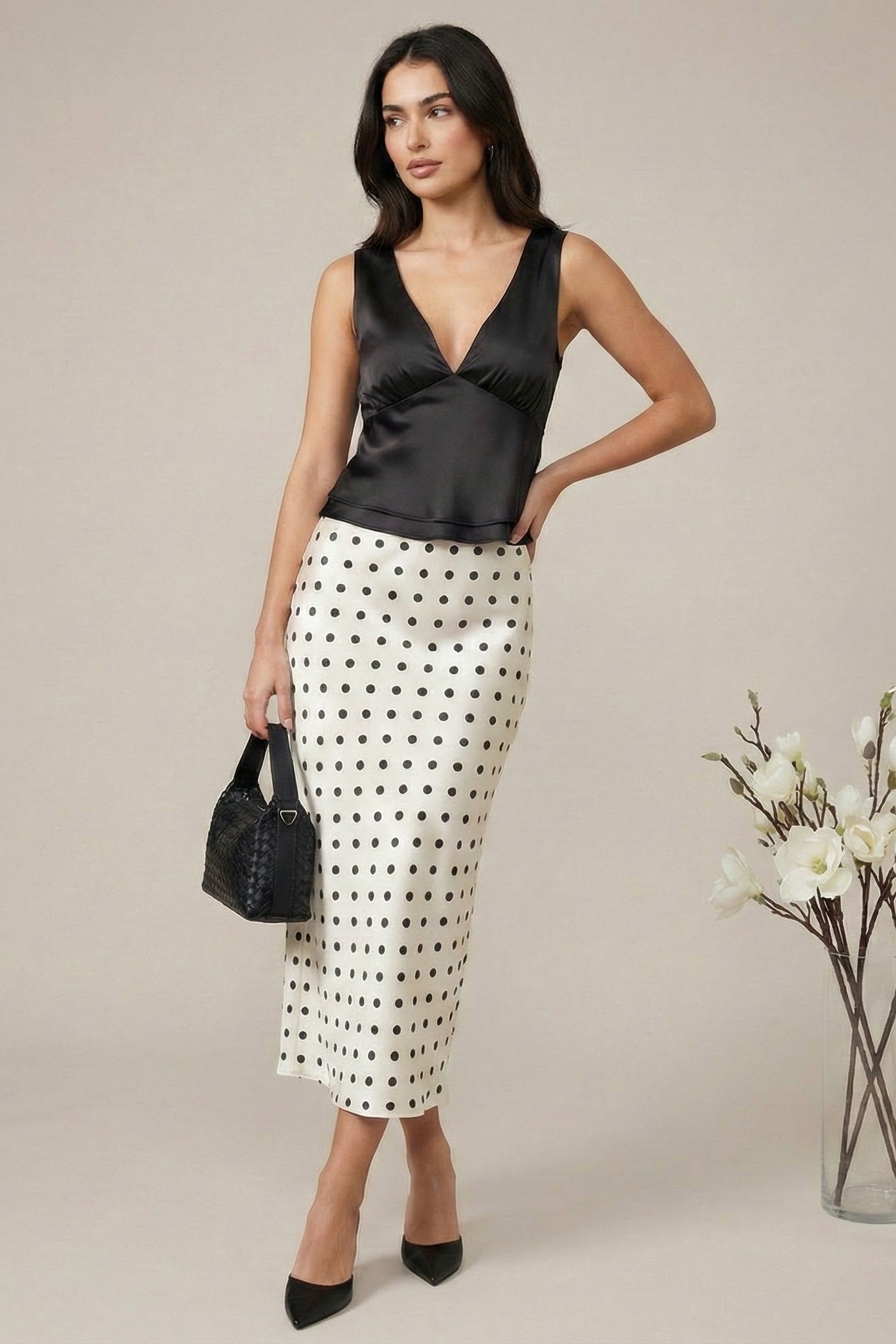 Woman wearing a black top and polka dot skirt with a vase of flowers on a neutral background