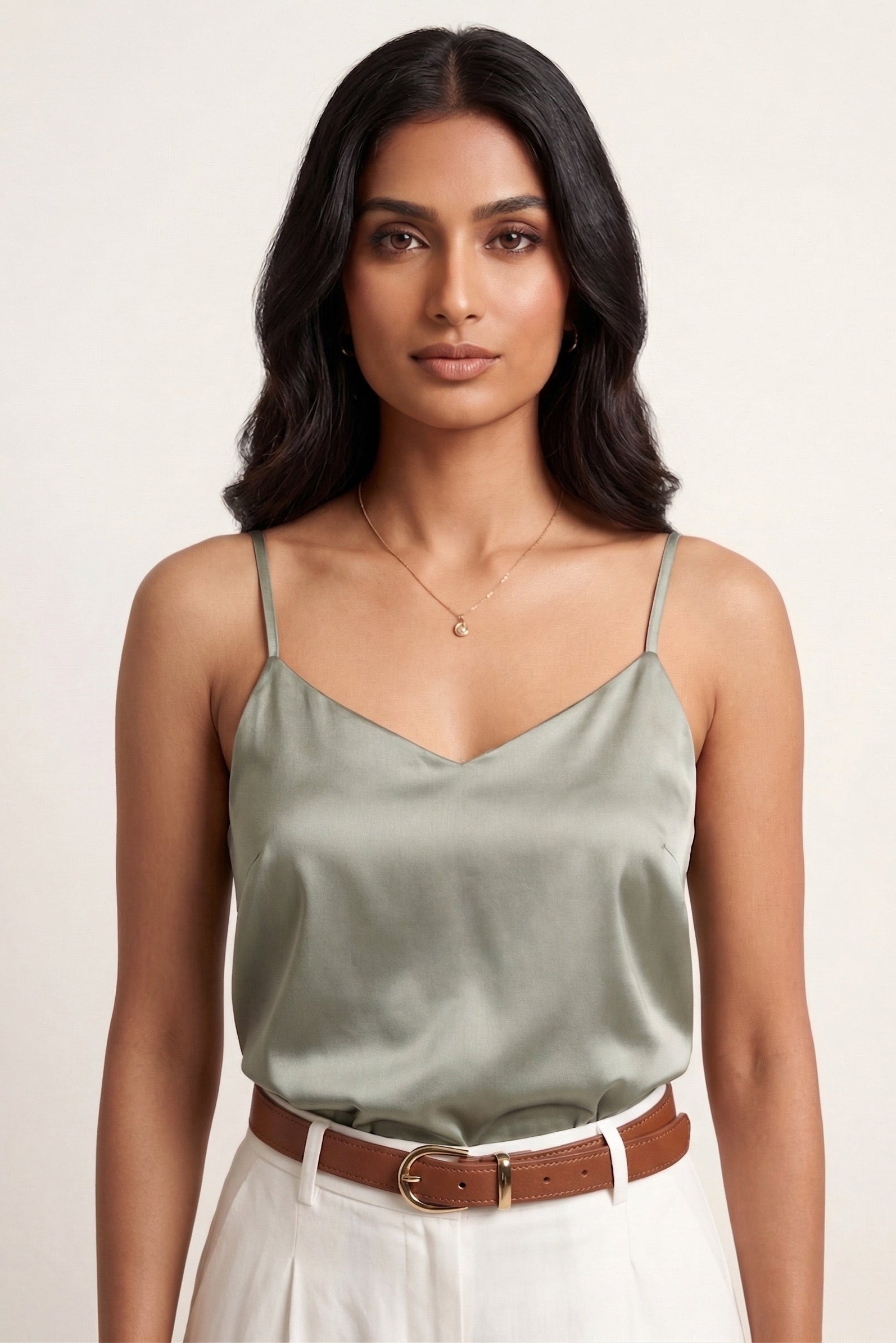 Woman wearing a green satin top and white pants with a beige background