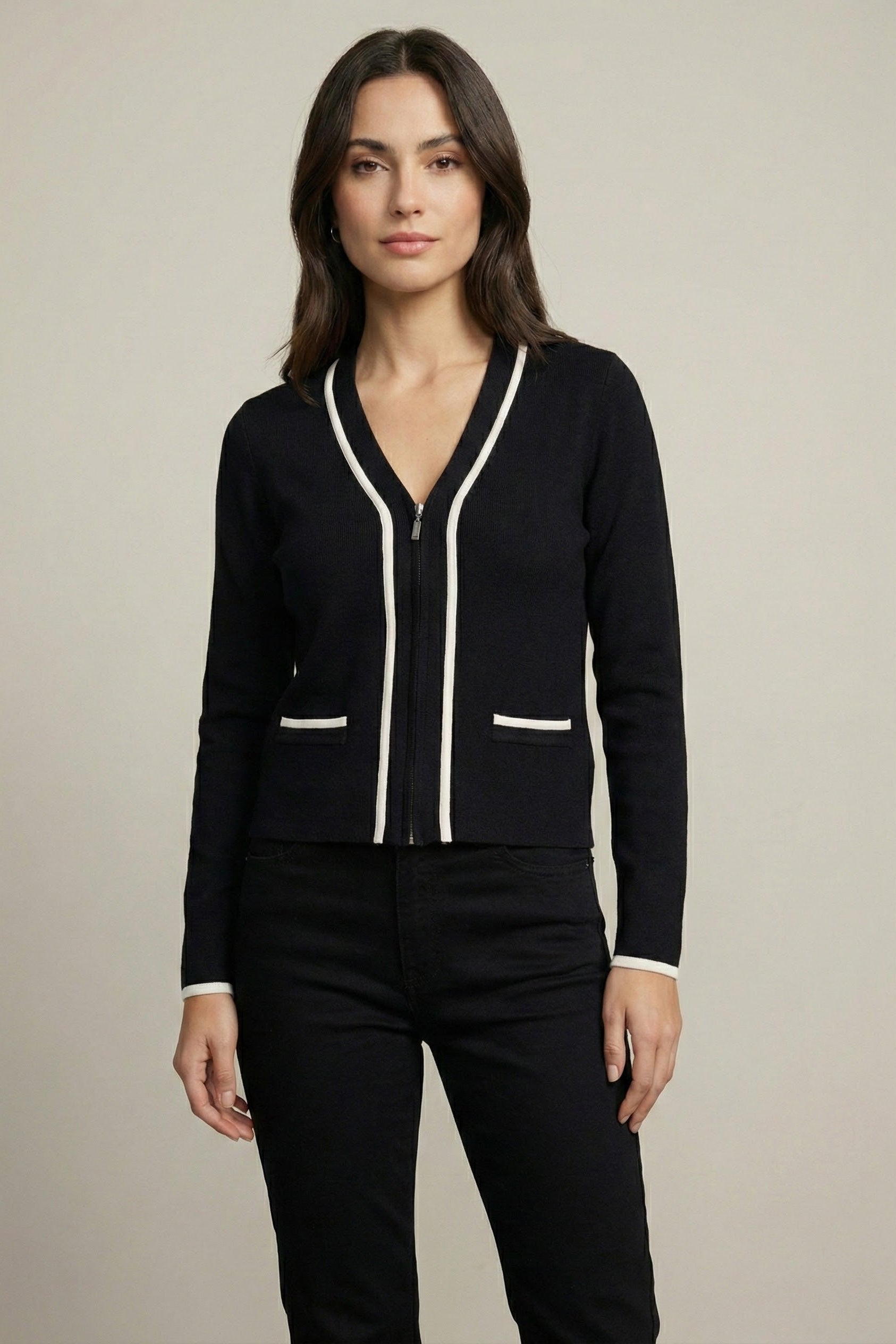 Woman wearing a black cardigan with white trim on a beige background