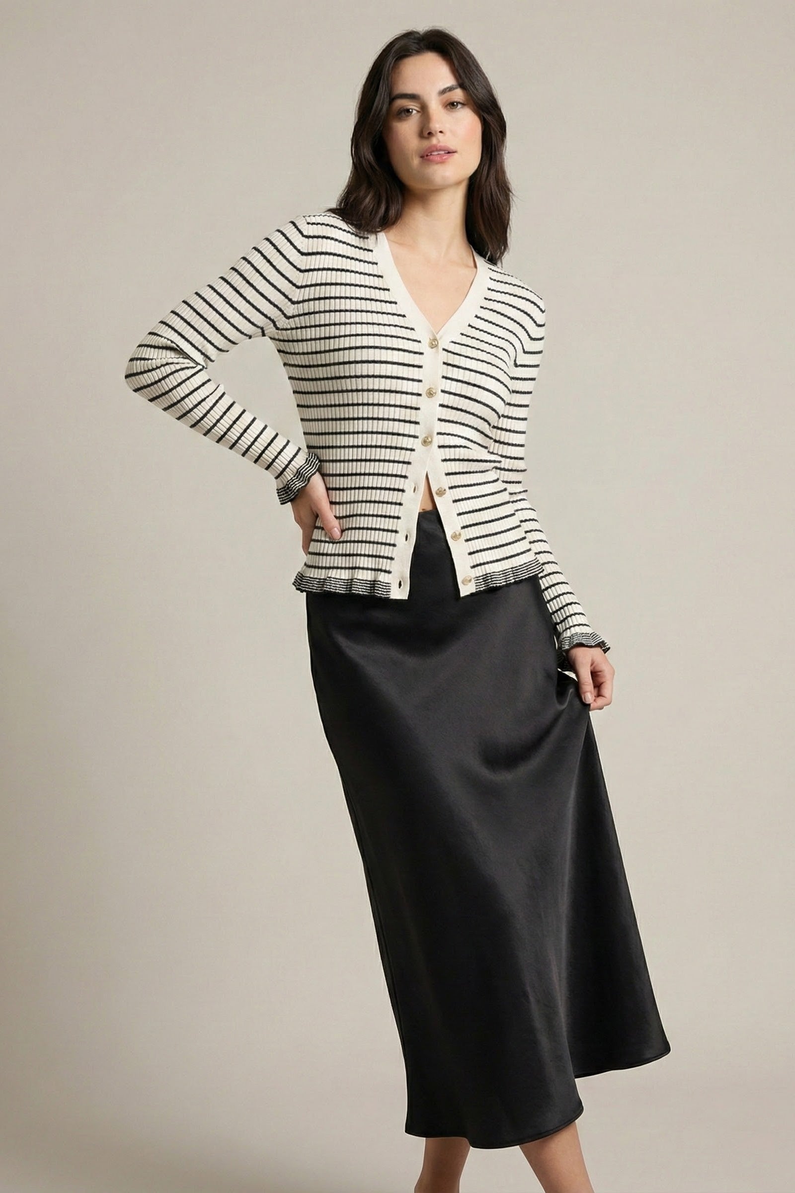 Woman wearing a striped cardigan and black skirt on a plain background