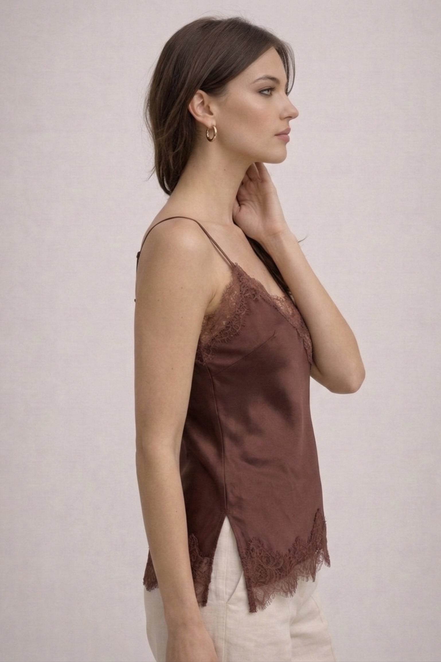 Woman wearing a brown lace-trimmed top against a plain background