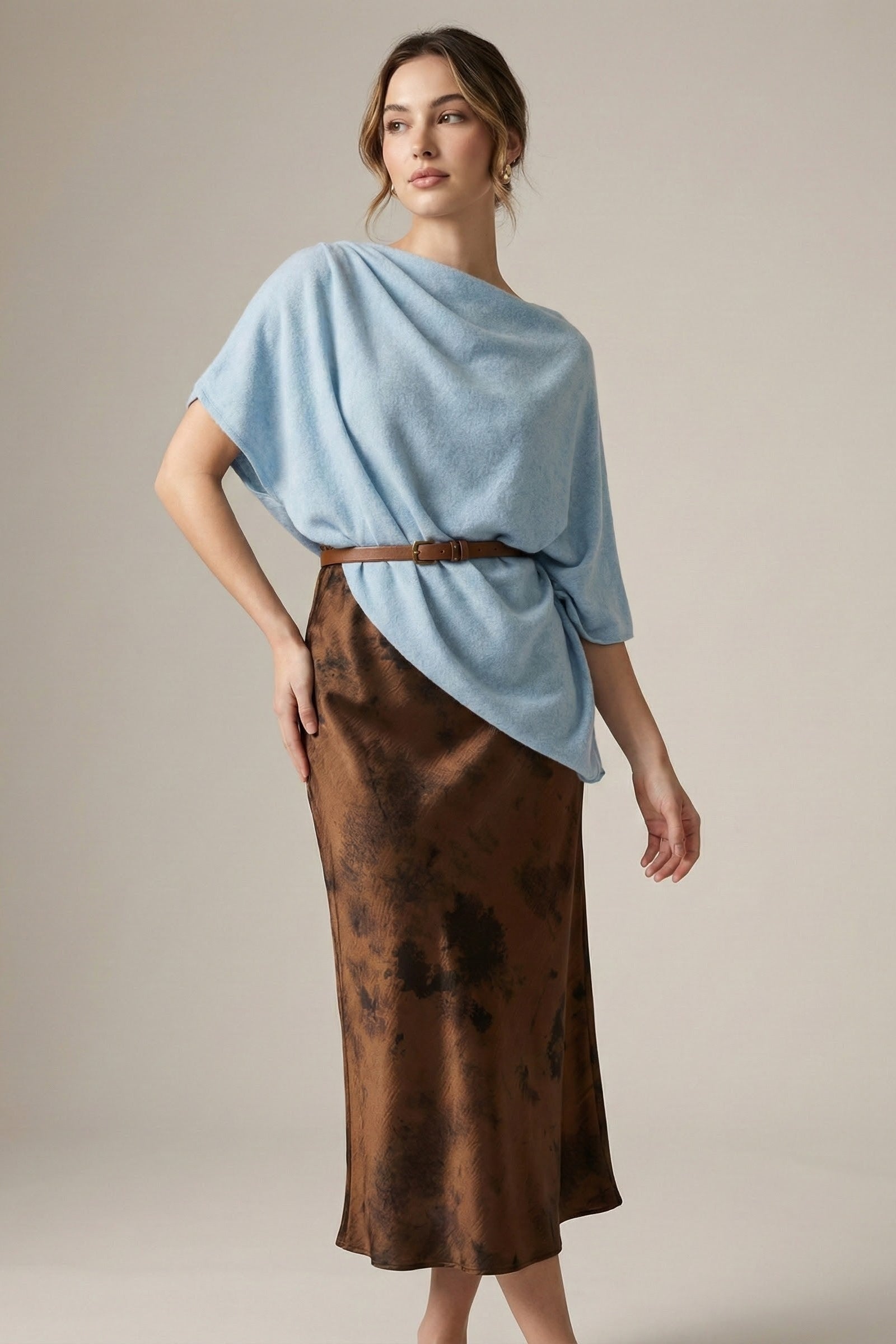 Woman wearing a light blue top and brown skirt against a neutral background