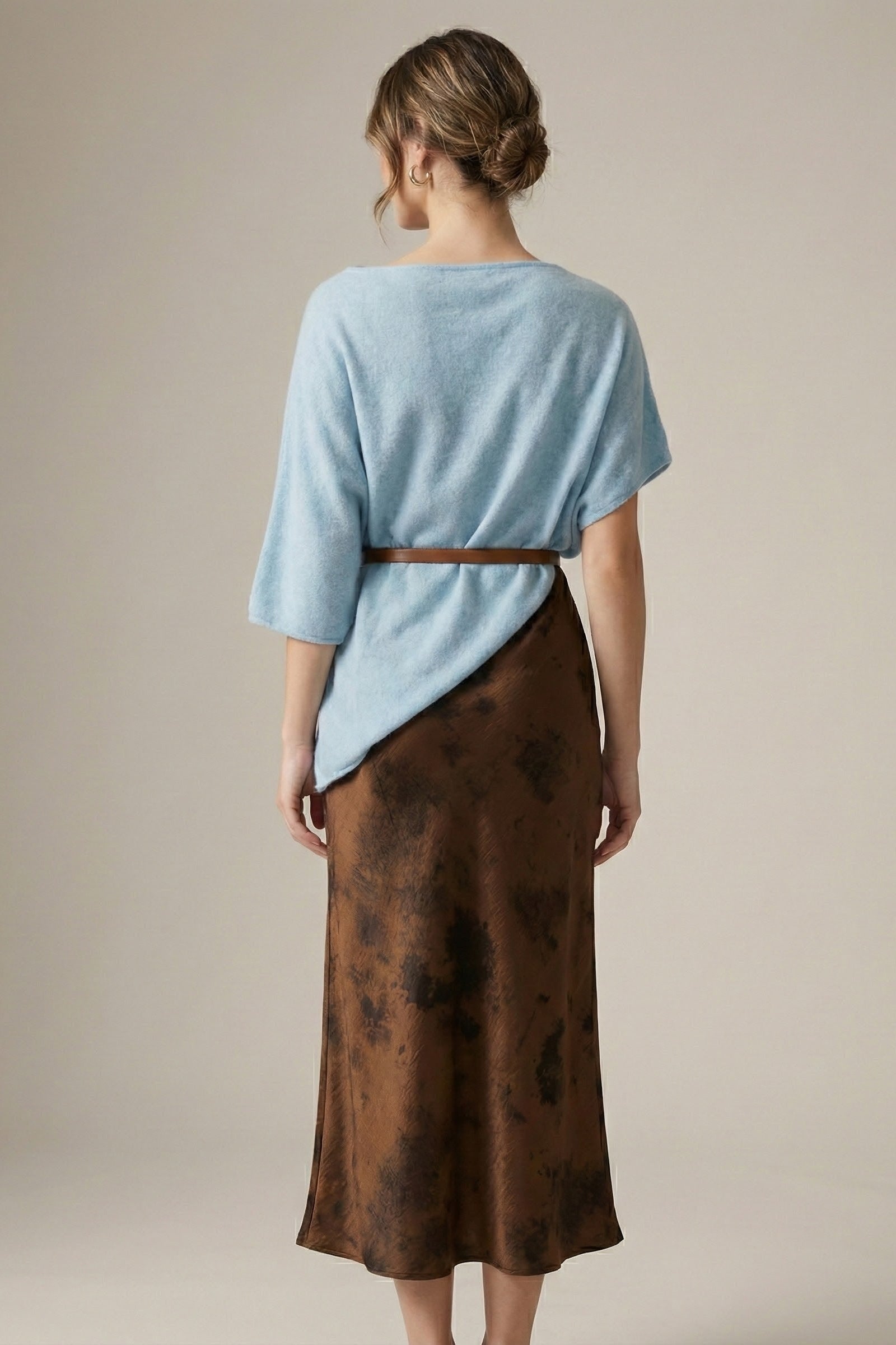 Woman wearing a light blue top and brown skirt against a neutral background