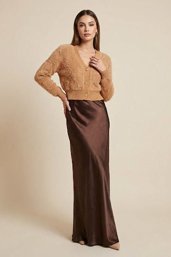 Woman wearing a brown cardigan and long brown skirt against a beige background