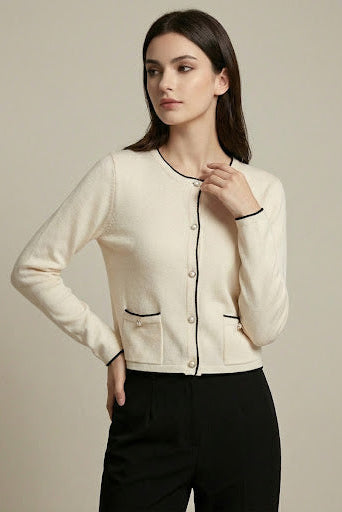 Woman wearing a cream-colored cardigan with black trim on a beige background