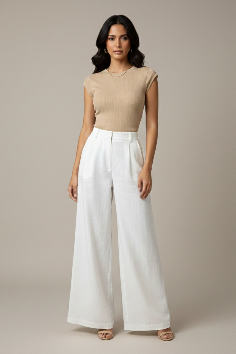 Woman wearing a beige sleeveless top and white pants against a neutral background