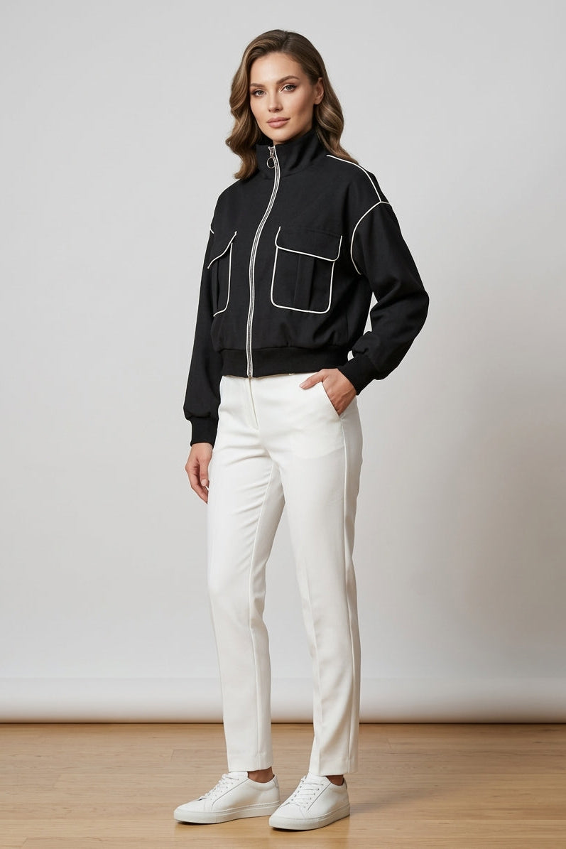 Woman wearing a black jacket with white accents and white pants against a plain background