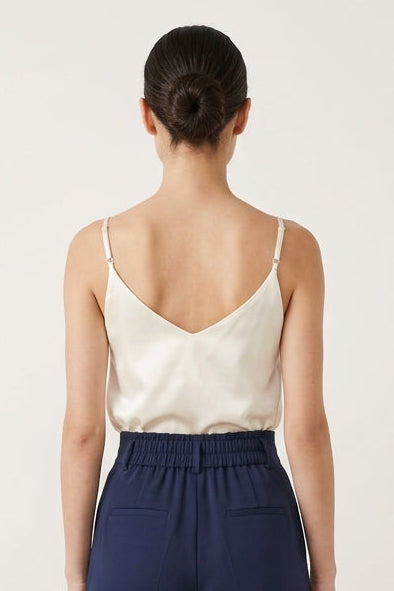 Woman wearing a cream top and navy pants on a white background