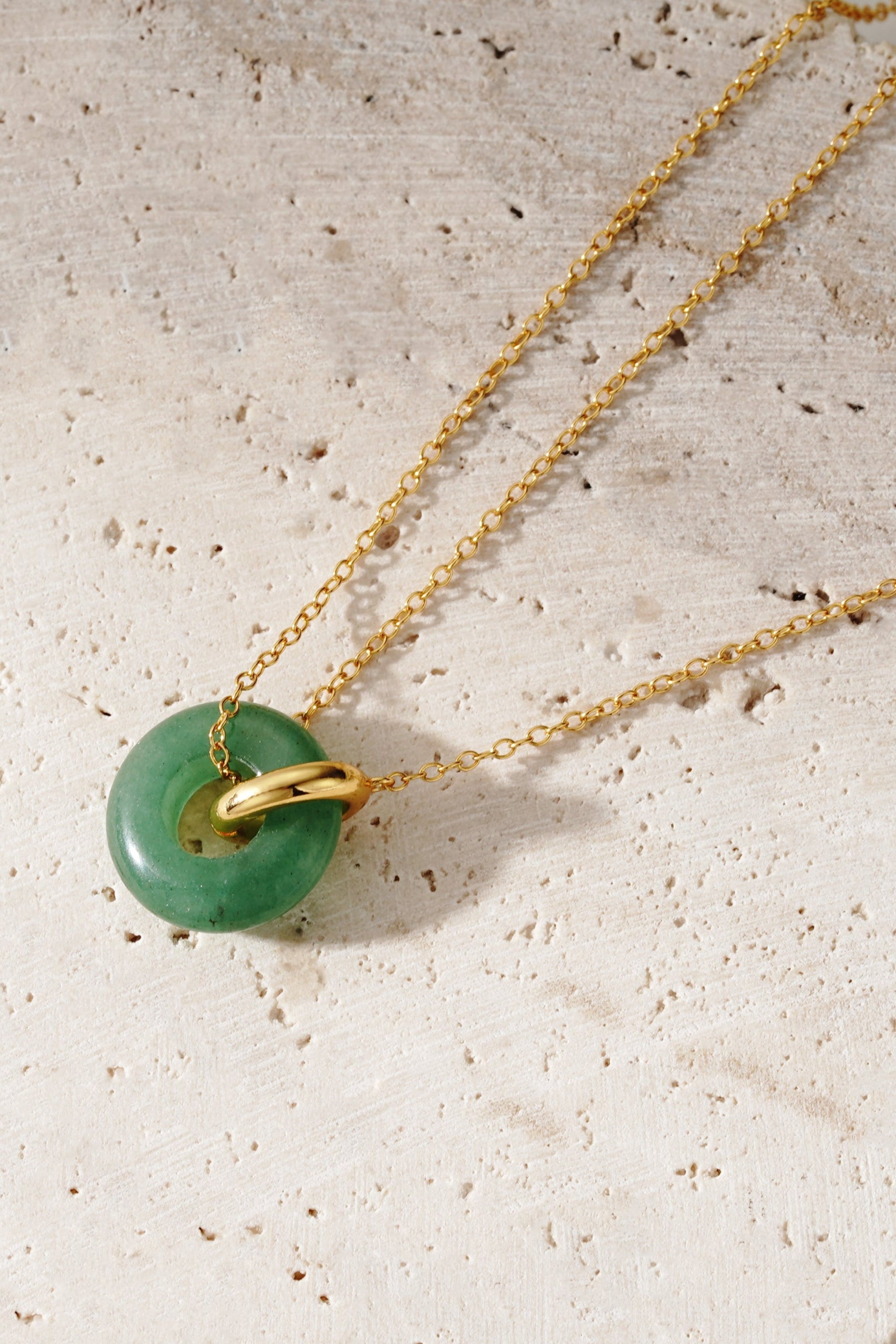 Gold necklace with a green pendant on a textured stone surface