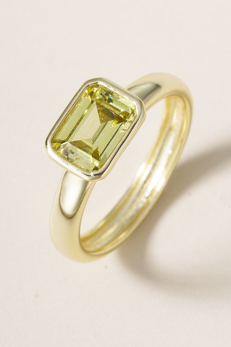 Gold ring with a green gemstone on a beige background