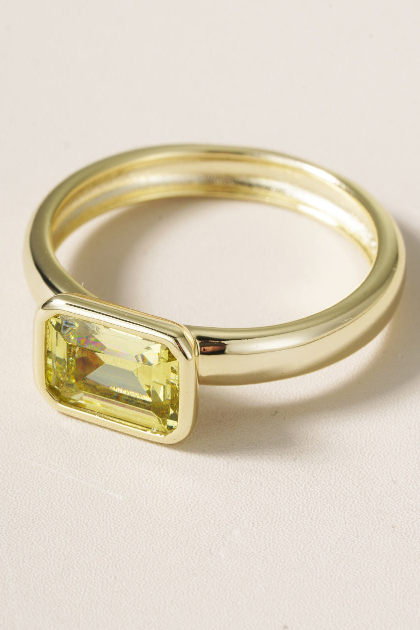 Gold ring with a yellow gemstone on a beige background
