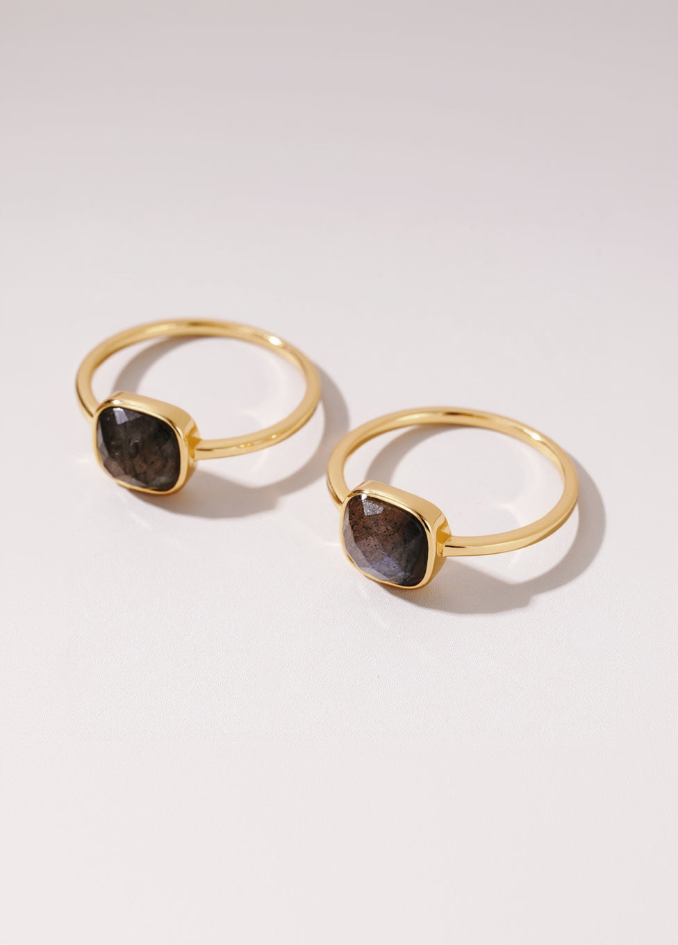 Two gold rings with brown gemstones on a light background