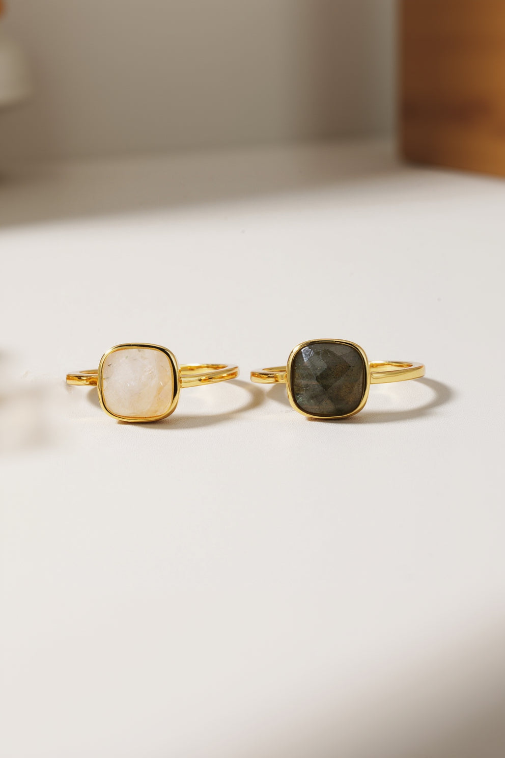 Two gold-rimmed rings with gemstones on a beige background