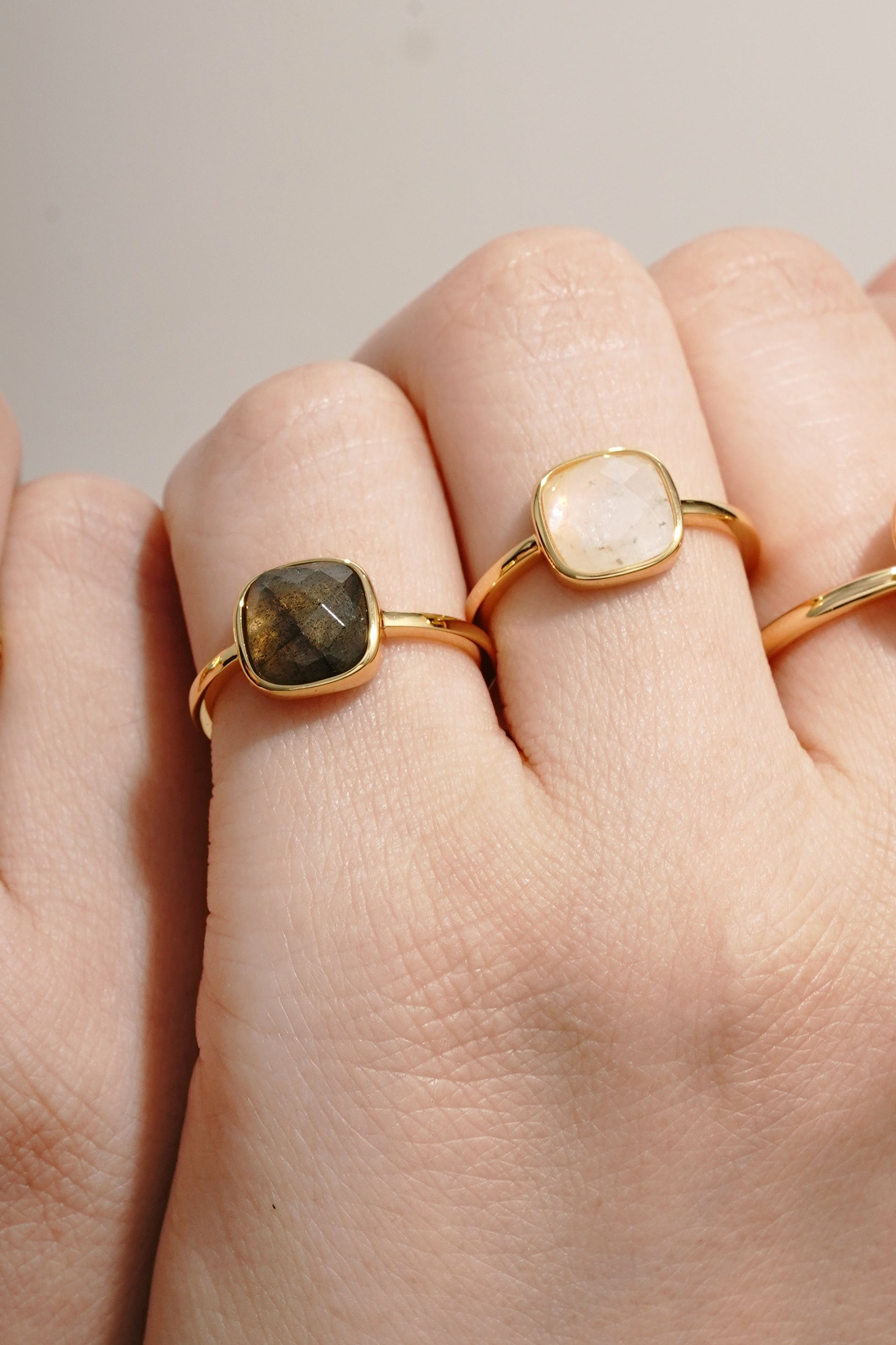 Hand wearing three gold rings with gemstones on a neutral background