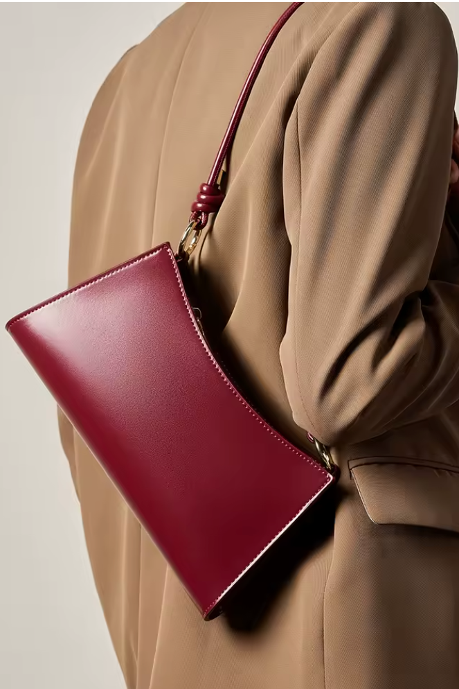 Red handbag held by a person wearing a beige coat against a neutral background