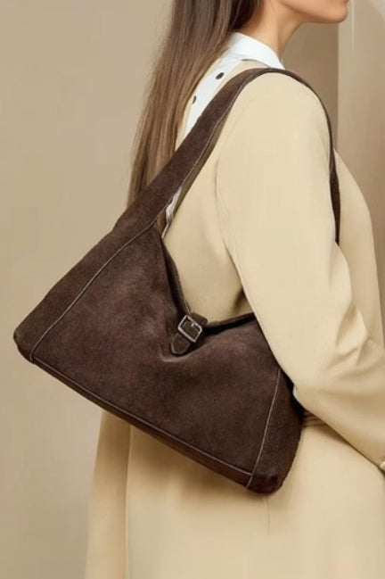Person holding a brown leather bag against a beige background