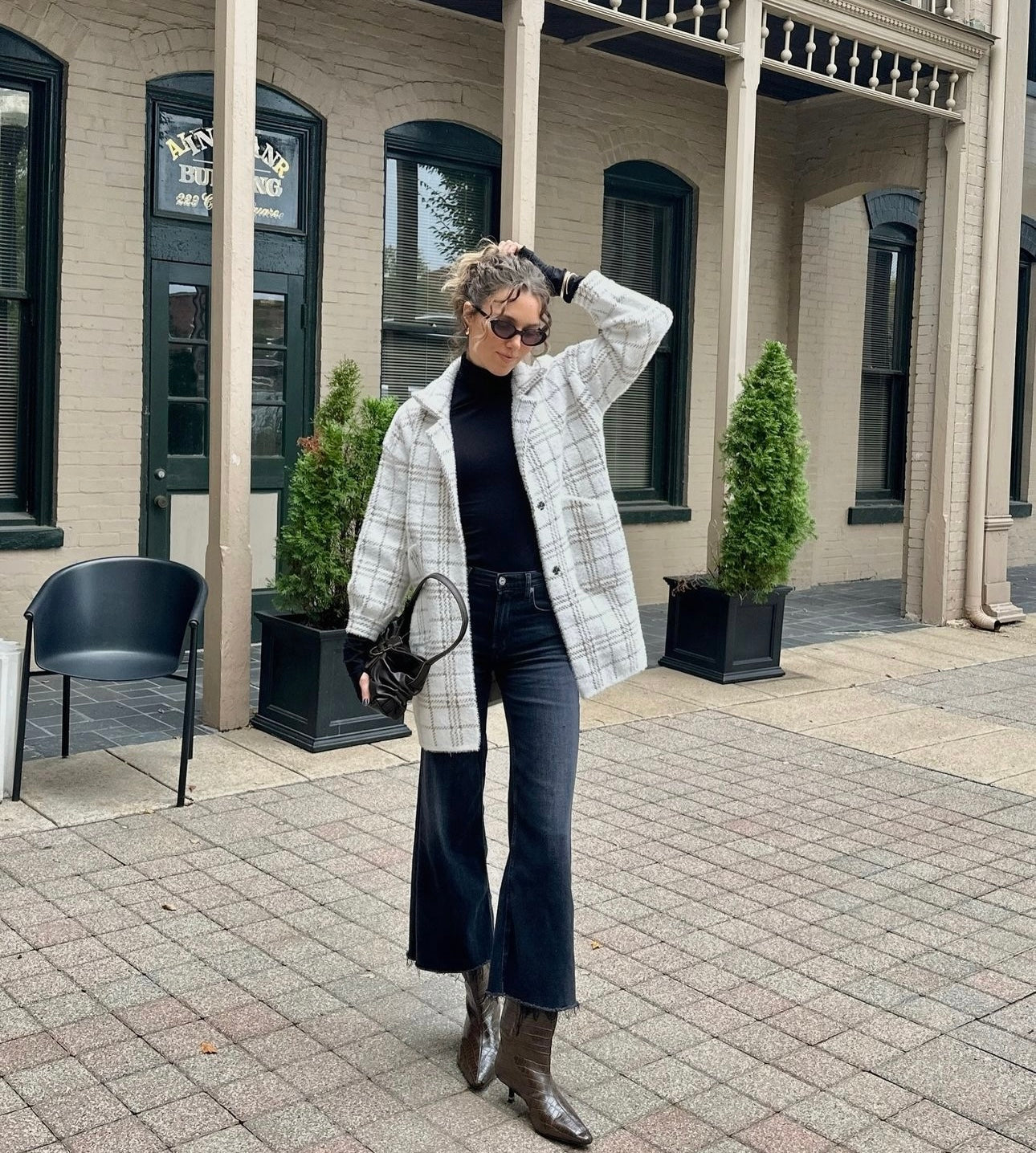 Woman in a plaid coat and black mock neck top standing in front of a building with potted plants