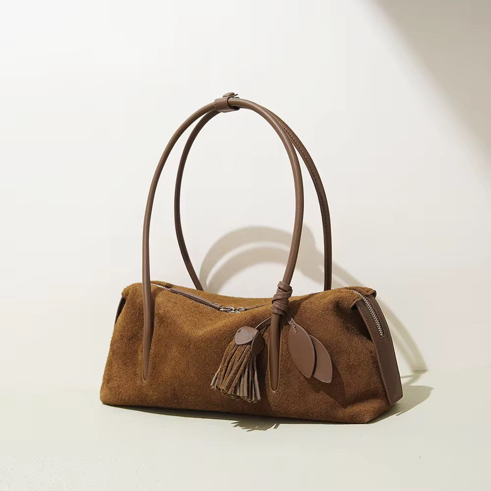 Brown suede handbag with leather handle and tassels on a light background